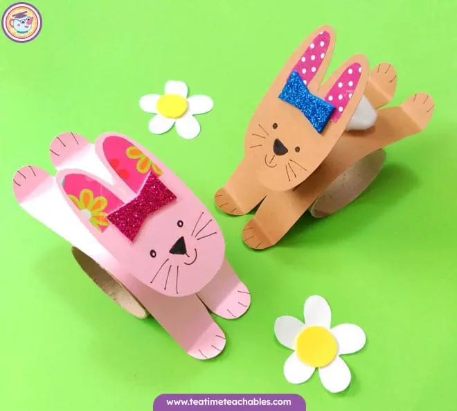 Two cute bunnies made from paper stand on a green background. This is a finished rabbit craft for kids.