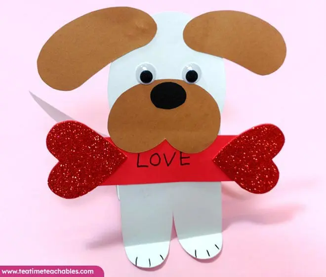 Easy Valentine craft for kids featuring a paper puppy with googly eyes and brown ears, holding red glitter hearts and displaying "LOVE." Pink background, playful.