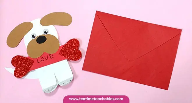 Easy Valentine craft for kids featuring a paper puppy with googly eyes and brown ears, holding red glitter hearts and displaying "LOVE." Pink background, playful.